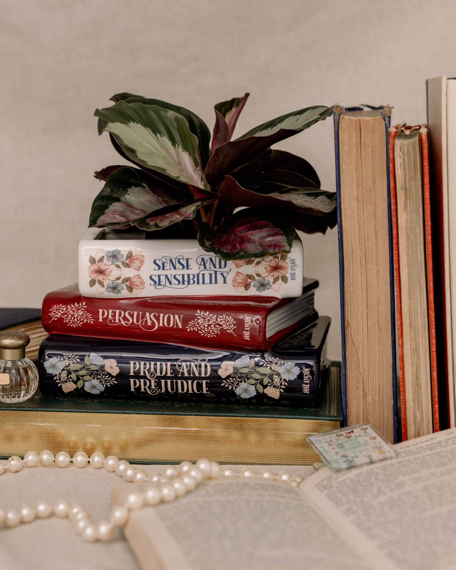 Stack of books with decorative covers, a plant, and pearls on a neutral background
