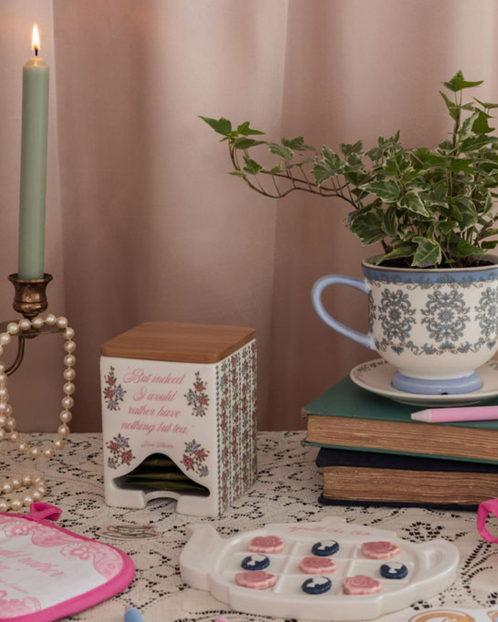 Decorative setting with a teacup, candle, books, and a plant on a table.
