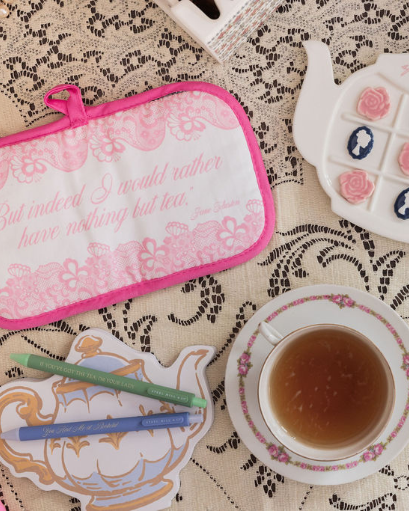Tea-themed items including a pot holder, teacup, and teapot on a lace tablecloth.