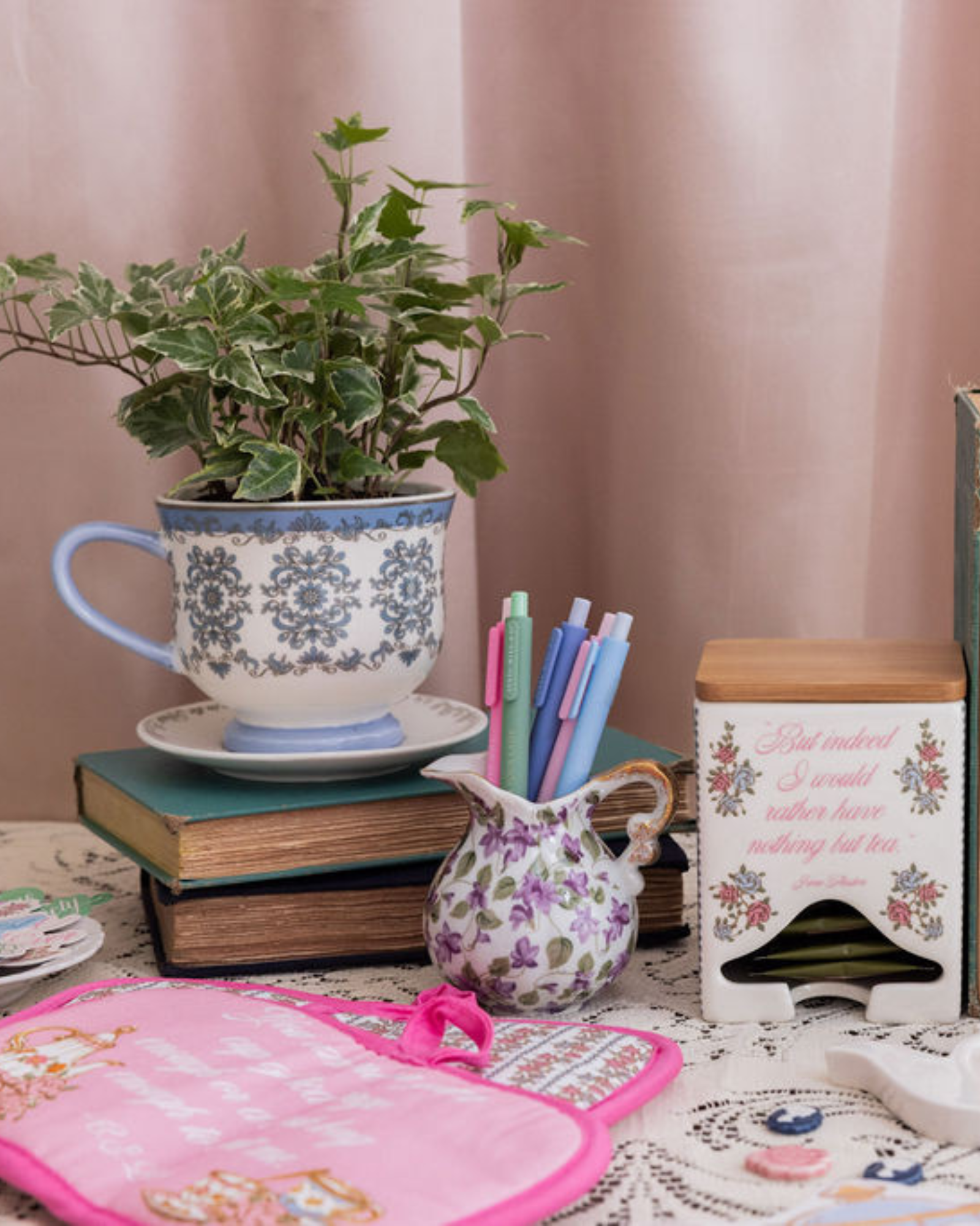 Decorative items including a teacup with plant, books, and a pink hot pad on a table.