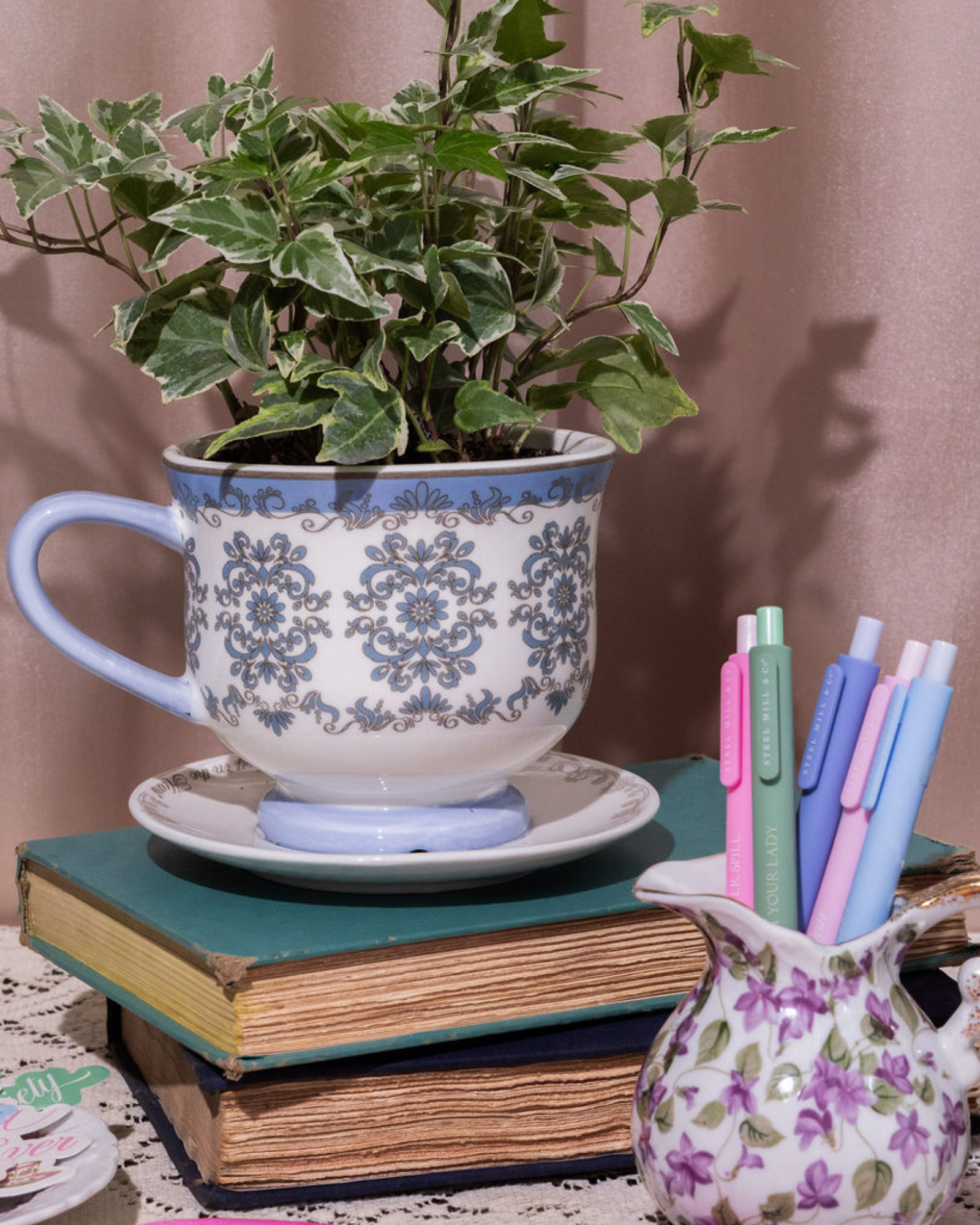 Decorative setup with a plant in a cup, books, and pens on a table.