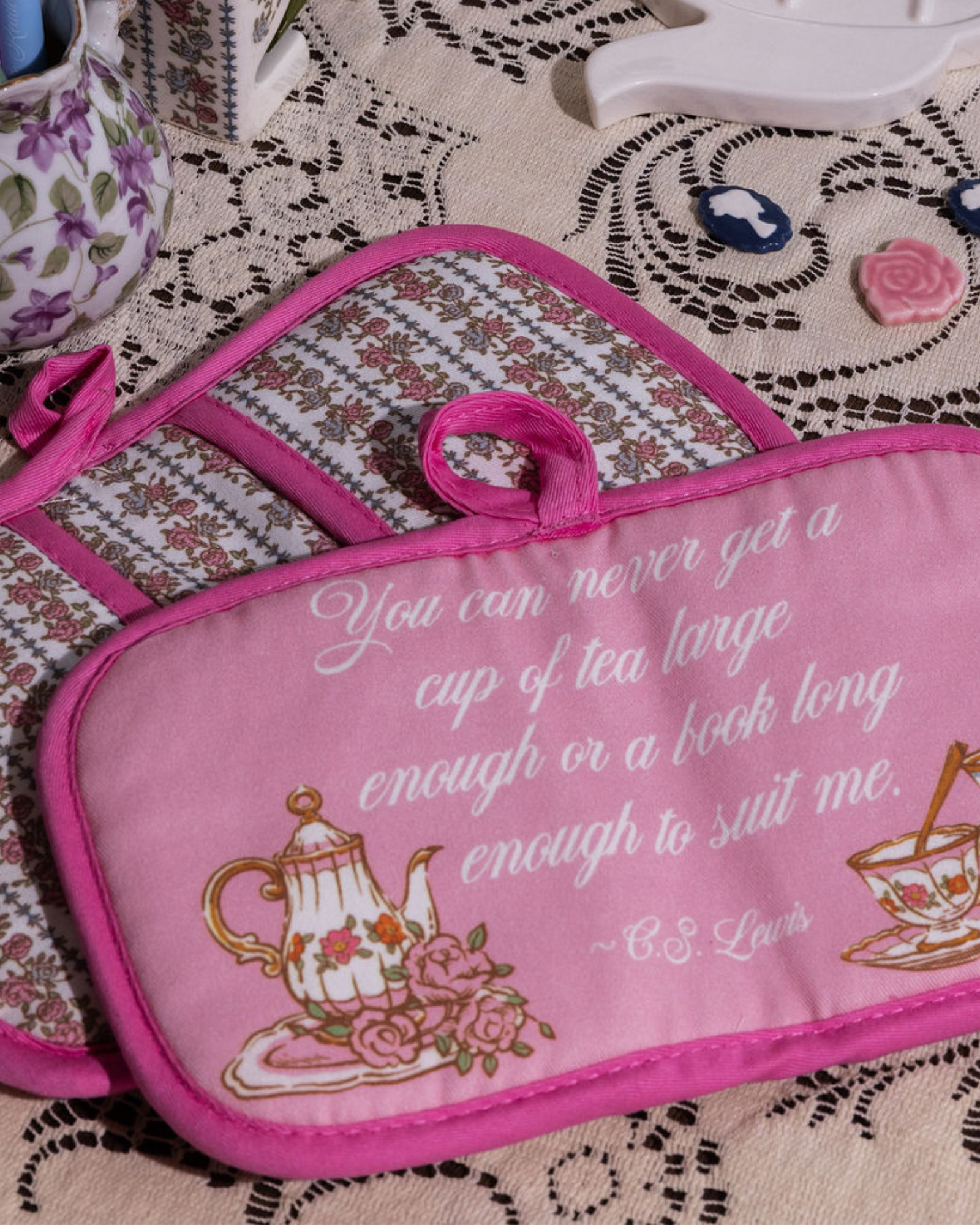 Pink potholder with tea-themed design and quote on a patterned surface