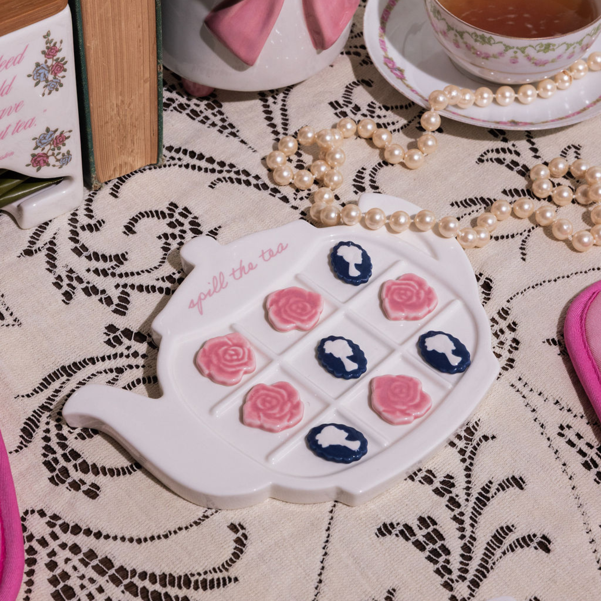 Teapot-shaped tic-tac-toe game with floral designs on a lace tablecloth