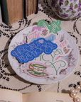 Decorative plate with colorful text and graphics on a lace tablecloth.