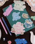 Teal notebook with decorative stickers on a wooden surface with tea-themed items.