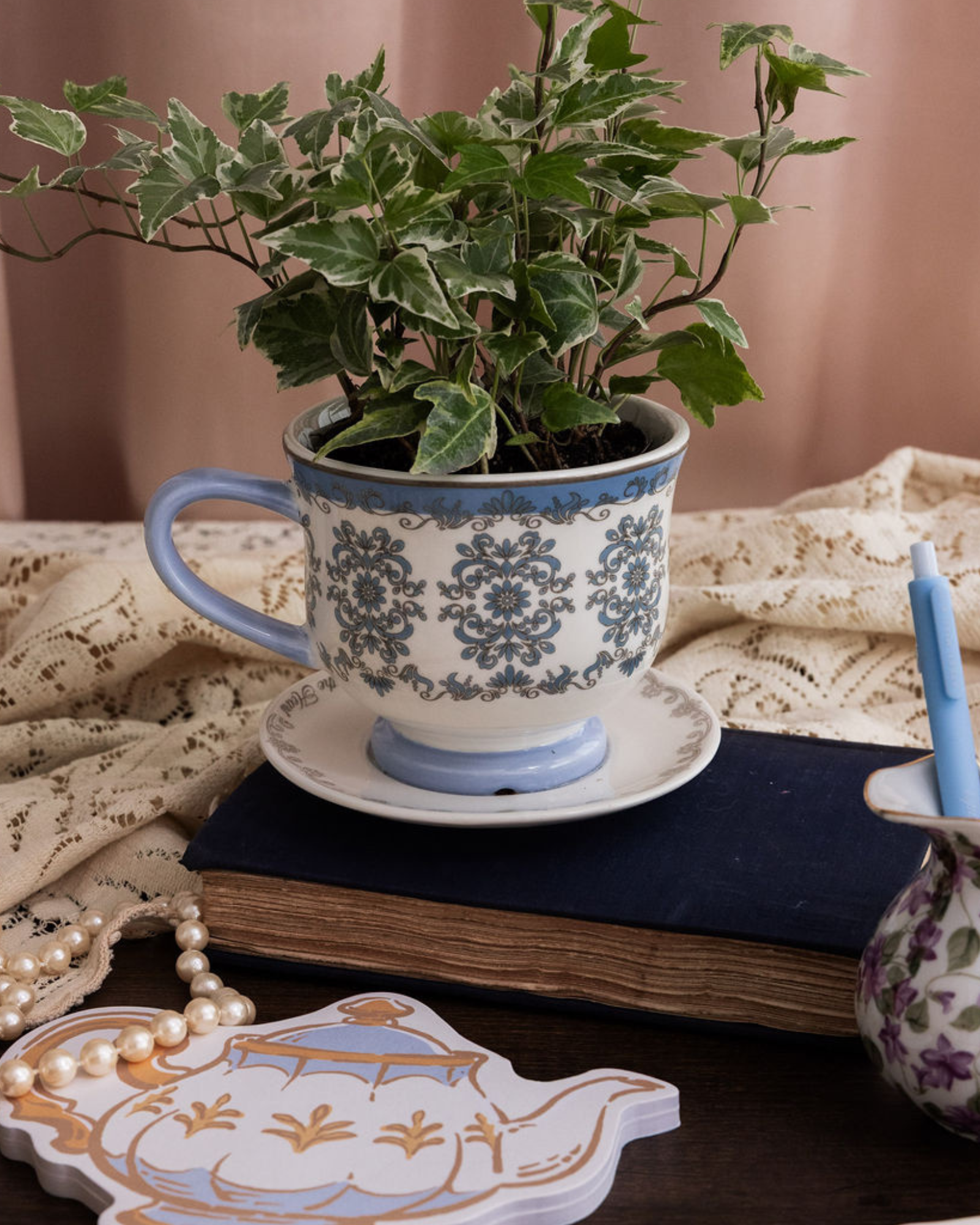 Decorative teacup with plant, notebook, and stationery on a table.