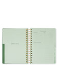 Open green planner with gold spiral binding on a white background