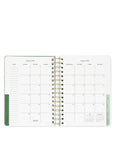 Open planner showing a monthly calendar layout with green binding on a white background