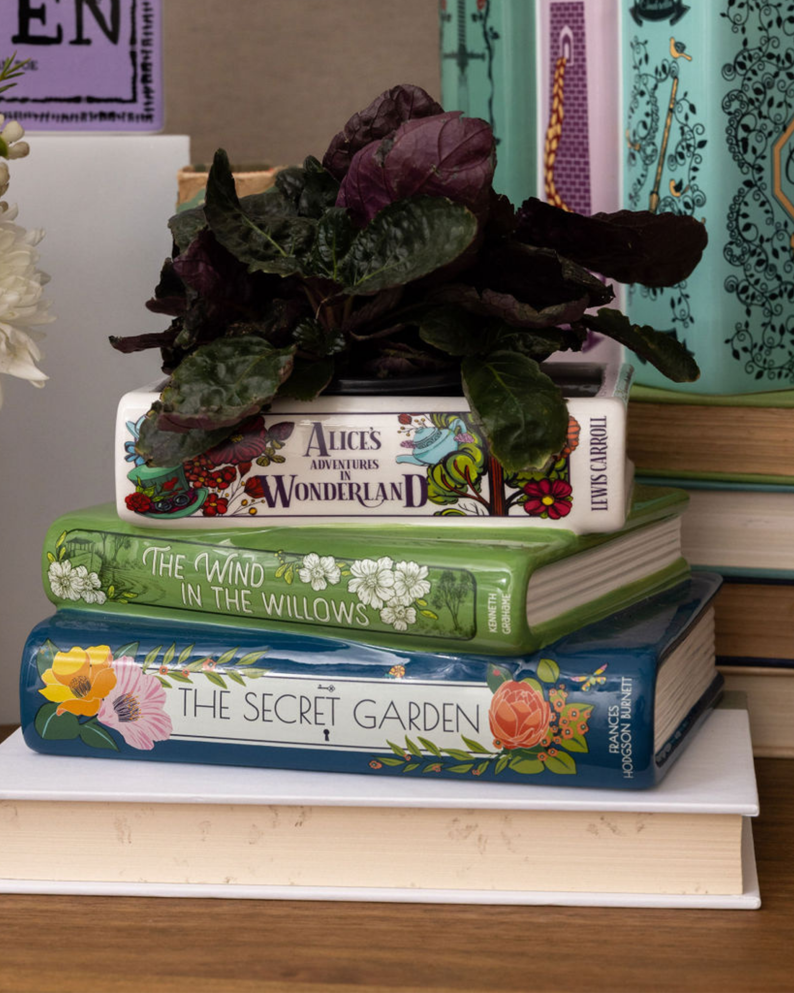 Stack of books with decorative covers on a white surface, surrounded by flowers and plants.