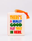 Ornament with 'THERE'S A REALLY GOOD PLOT TWIST IN HERE' and an orange hanger on a white background