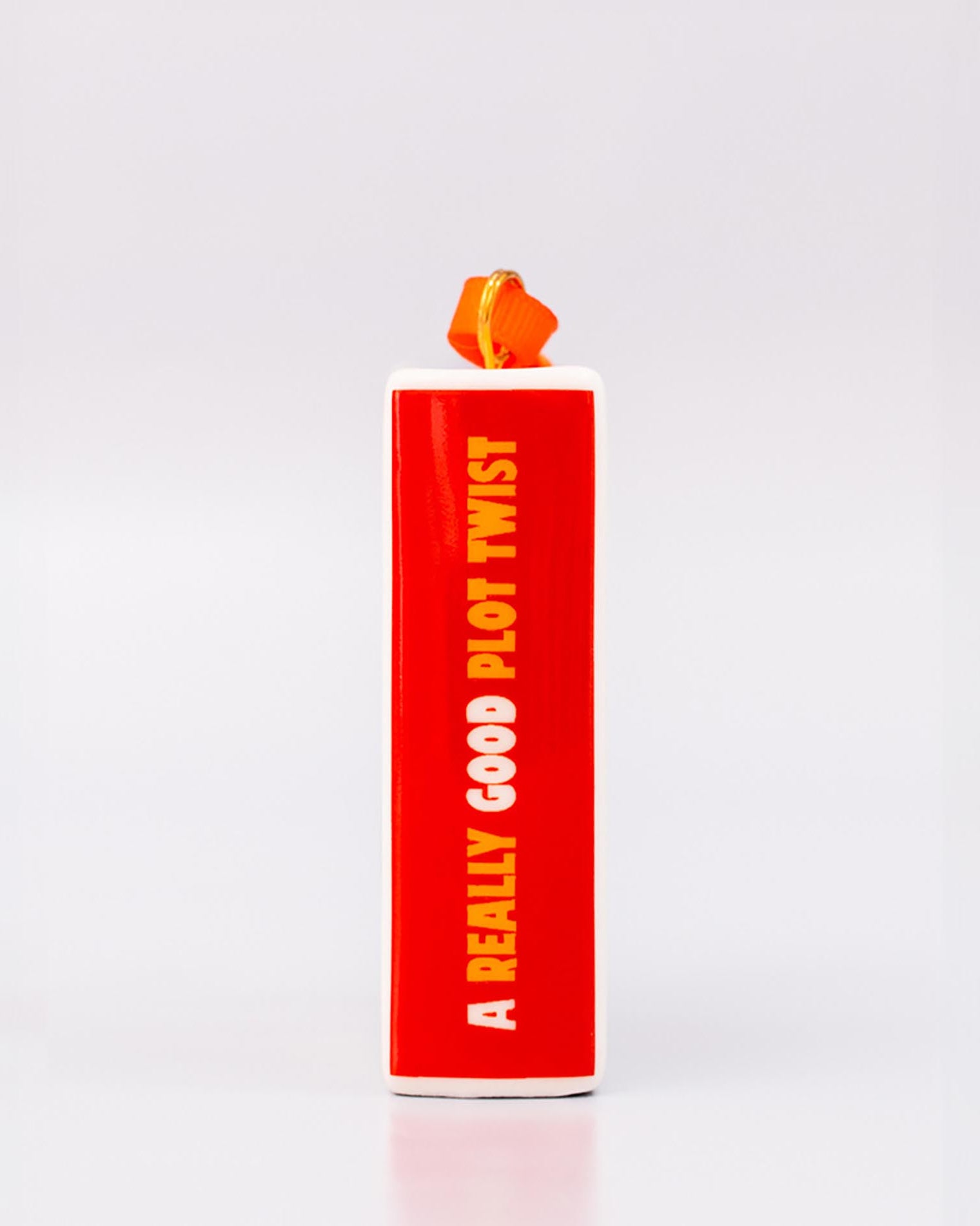 Spine of ornament with 'THERE'S A REALLY GOOD PLOT TWIST IN HERE' and an orange hanger on a white background