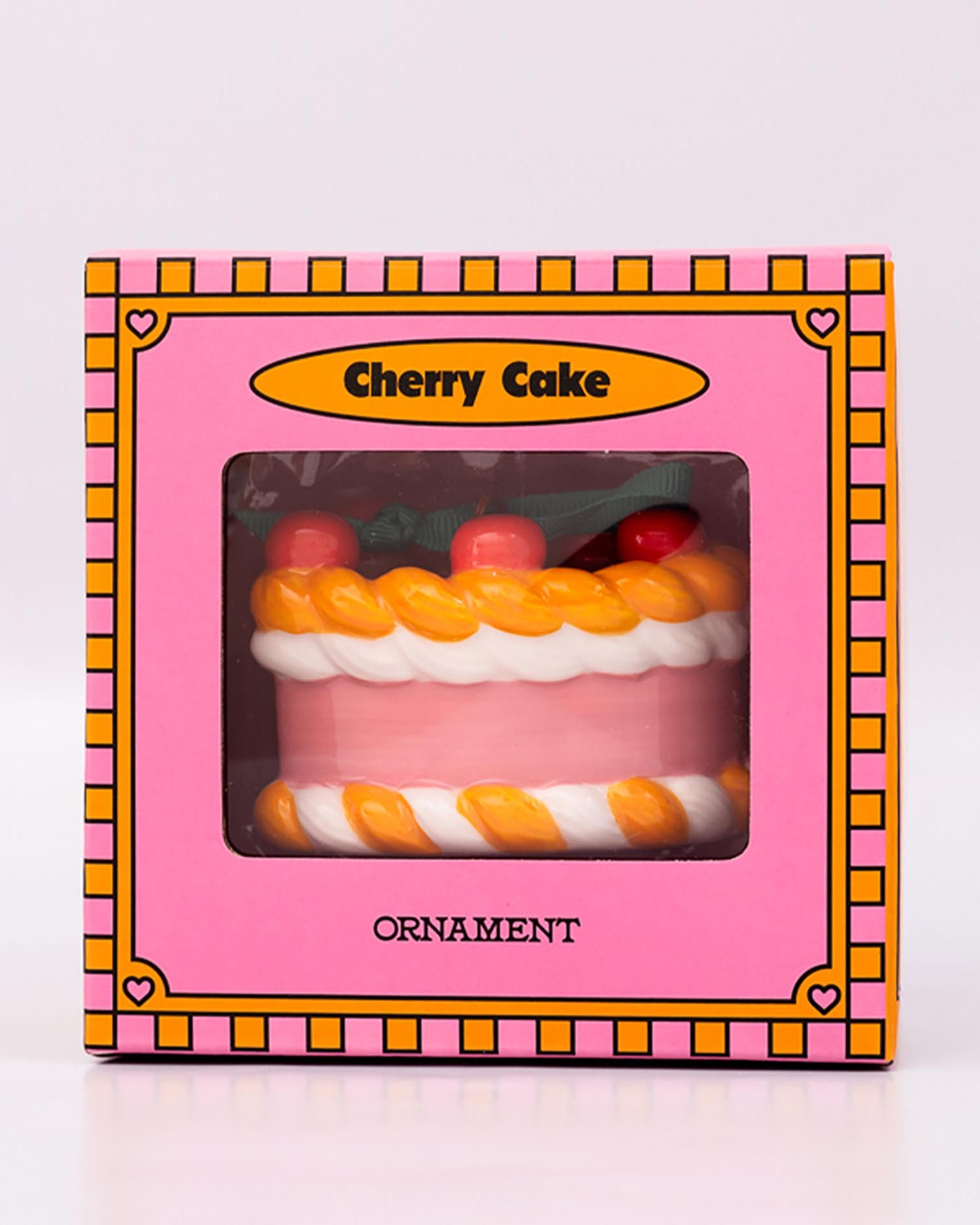 Packaged ornament cake with pink filling, orange and white striped sides, and red cherries on a white background