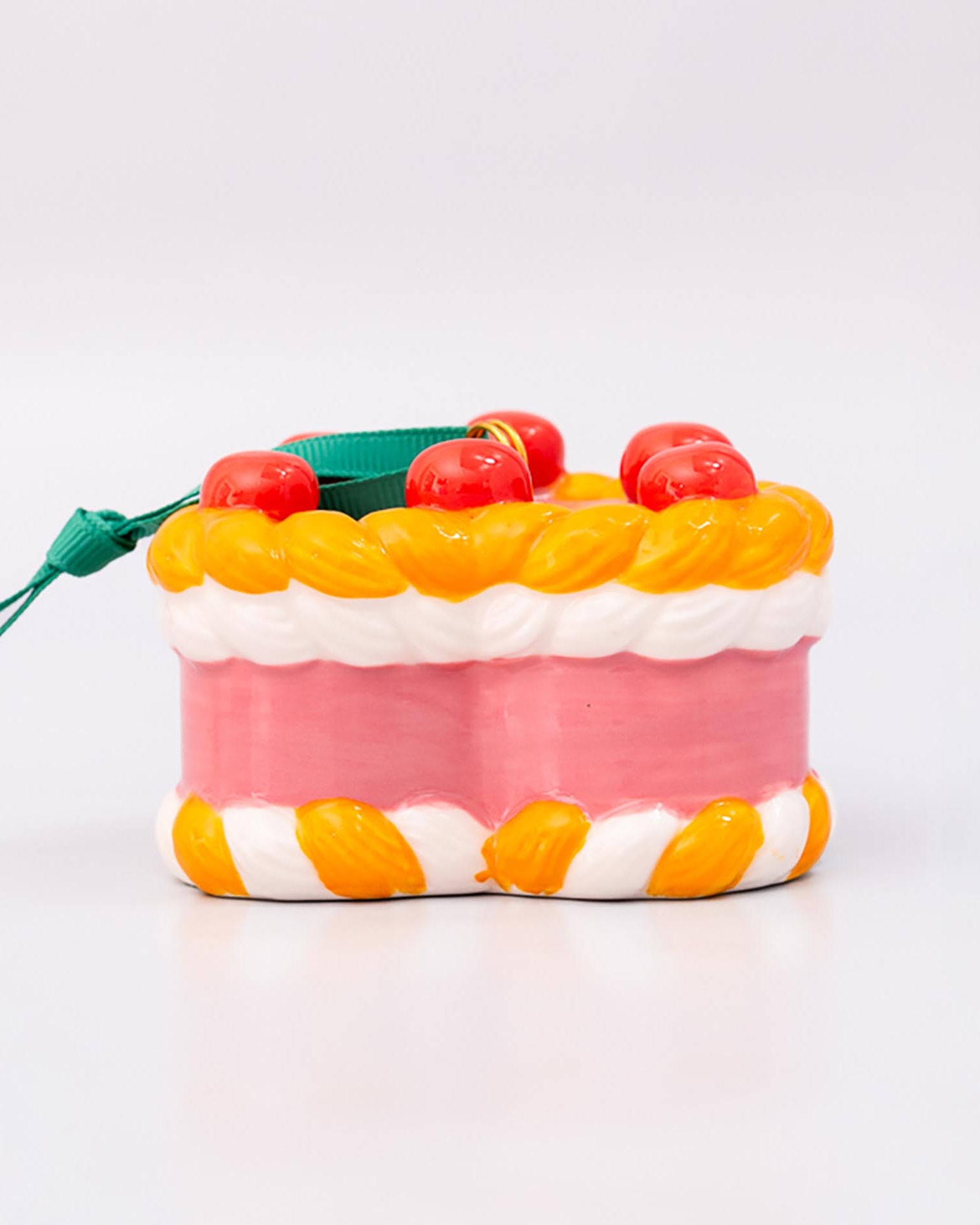 Sideview of ornament cake with pink filling, orange and white striped sides, and red cherries on a white background