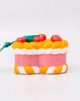 Sideview of ornament cake with pink filling, orange and white striped sides, and red cherries on a white background