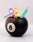 Black ball-shaped holder with number 8 holding colorful stationery items on a light gray background