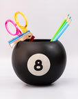 Black billiard ball-shaped holder with number 8 holding stationery items on a white background