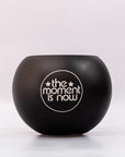 Black bowl with 'the moment is now' text on a white background