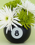 Black vase with number 8 and white and green flowers on a light green background