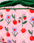 Pink quilted bag with cherry and flower pattern and green ribbon on a light gray background