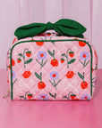 Pink quilted bag with floral and fruit patterns and a green bow on a pink background