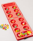 Red checkered mancala board with fruit-themed items on a light gray background