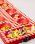 Up close of red checkered mancala board with fruit-themed items on a light gray background