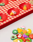Up close of pieces of red checkered mancala board with fruit-themed items on a light gray background