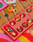 Red checkered mancala board with fruit-themed items on a light gray background
