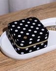 Black polka dot jewelry box with gold zipper on a white tray