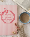 Pink notebook with decorative bow and text on a white background