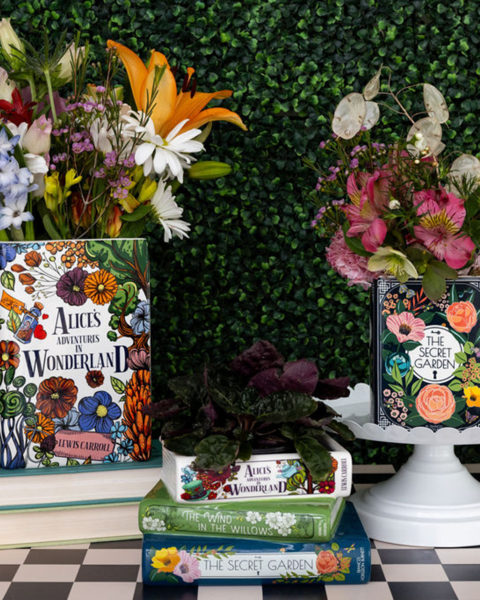 Books with floral designs on covers displayed against a green bush background.
