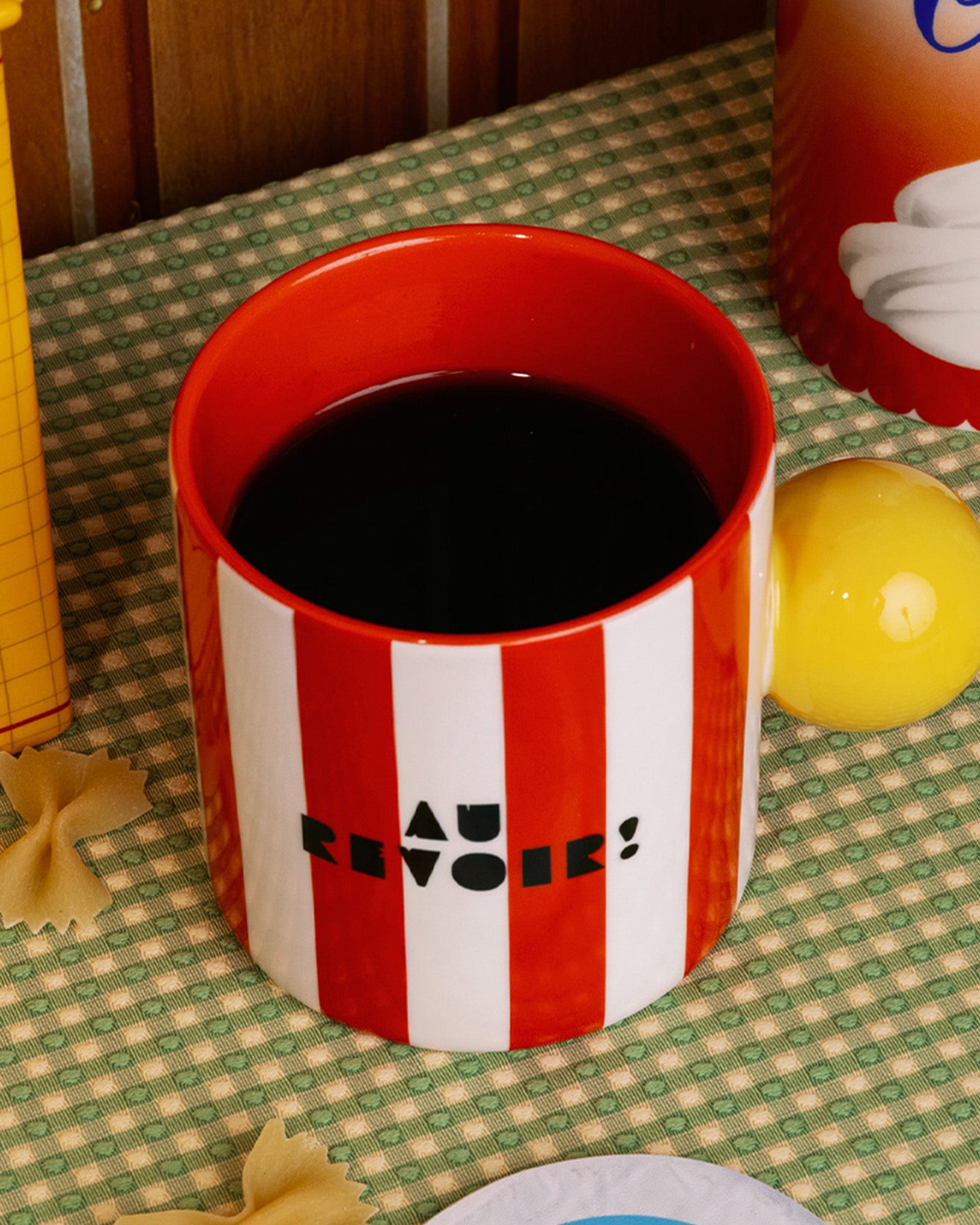 top view of red and white vertical stripe mug with yellow ball handle and double sided typography with 'BONJOUR!' on one side and 'AU REVOIR' on the other