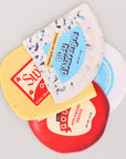 Side view of four different types of cheese coasters with labels on a light gray background