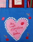 Blue tote bag with pink heart design and text 'The Smell of Pastries & Books' on a red background.