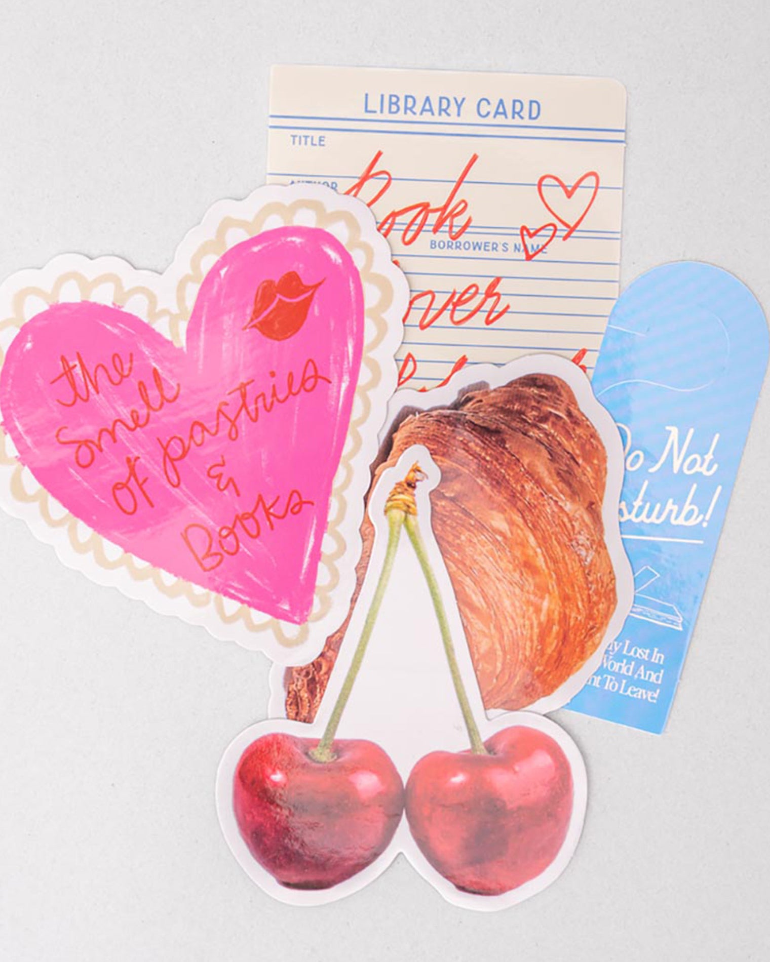 Set of colorful stickers with heart, cherry, library card, pastry, and bookmark on a light gray background.