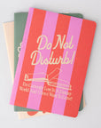 Notebook with 'Do Not Disturb! I'm Currently Lost In A Fantasy World And I Don't Want To Leave!' text on a gray background