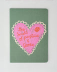 Notebook with pink heart design and text on a green background