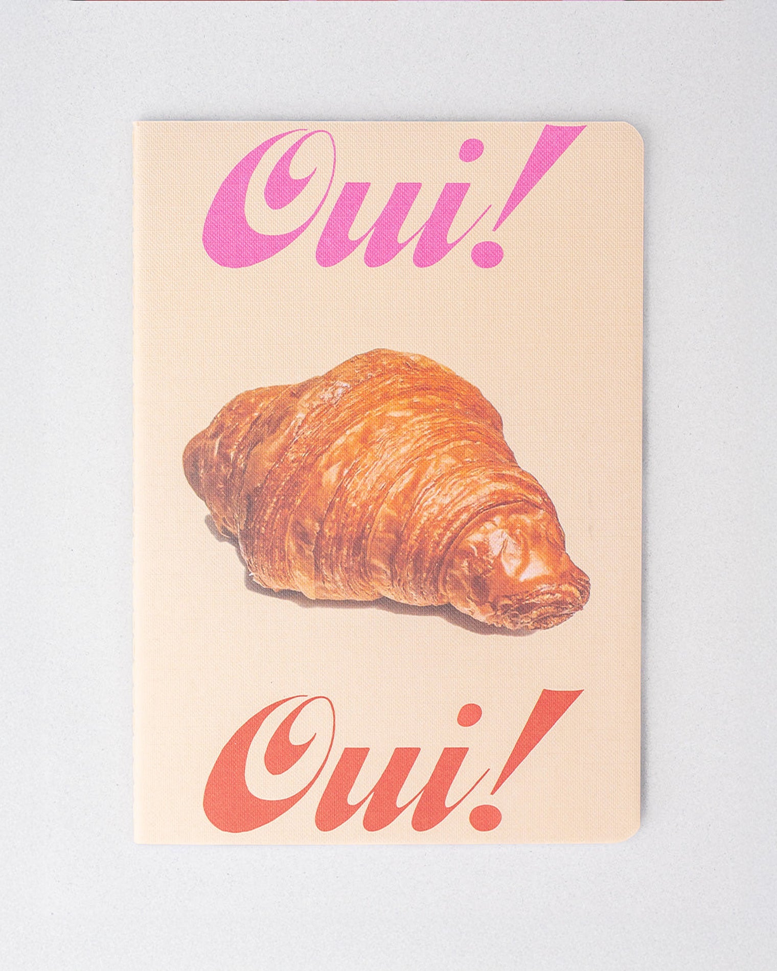 Notebook with a croissant and 'Oui!' text on a light background
