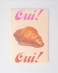 Notebook with a croissant and 'Oui!' text on a light background