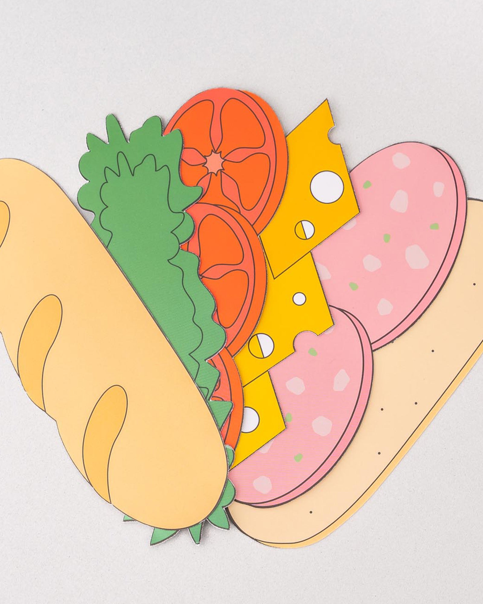 Colorful paper cutout of a sandwich with bread, lettuce, tomato, cheese, and meat on a light gray background
