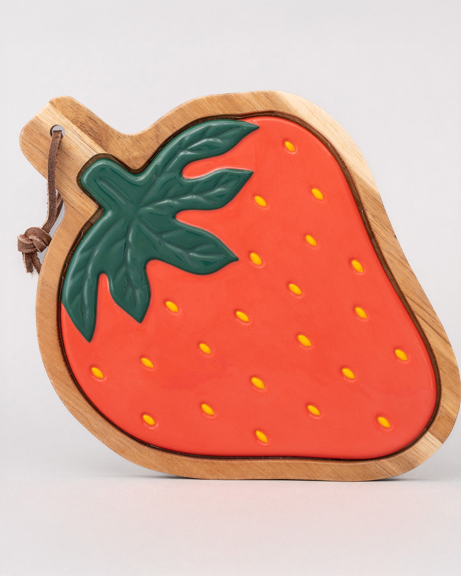 Strawberry-shaped wooden trivet with a green leaf on a light gray background
