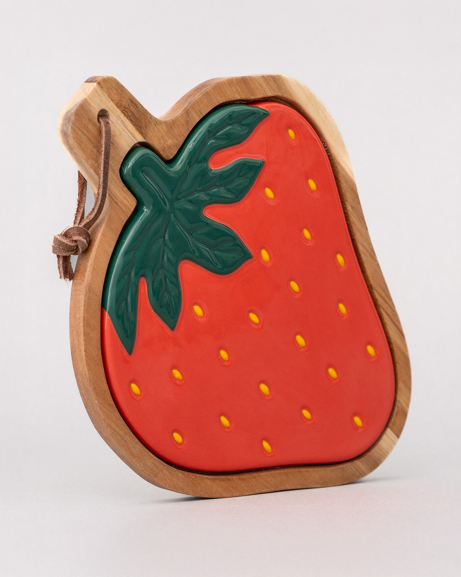 side view of Strawberry-shaped wooden trivet with a green leaf on a light gray background