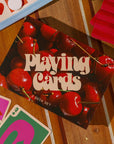 Box of playing cards with cherry design on a wooden surface