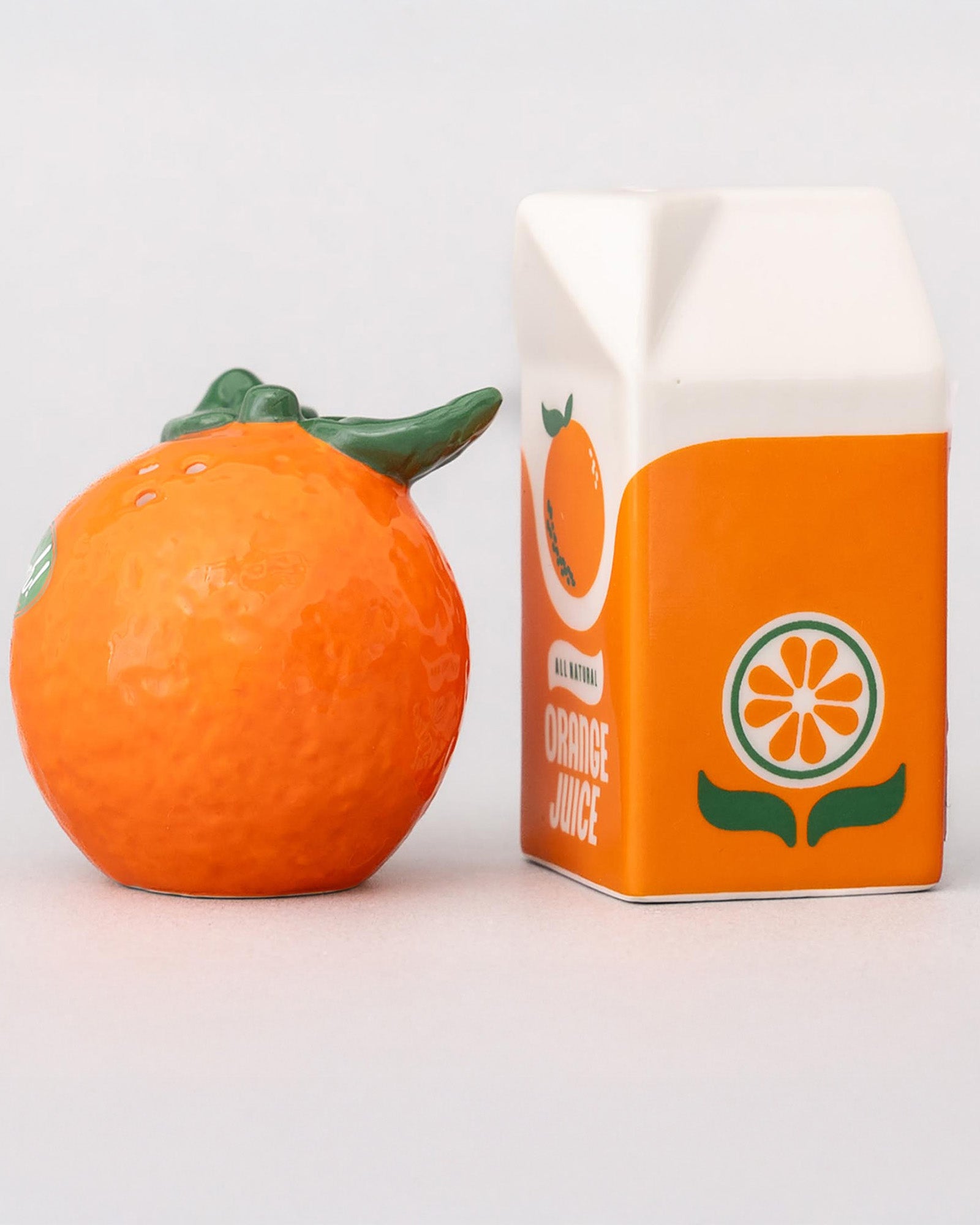 Orange fruit next to a carton of orange juice on a light gray background