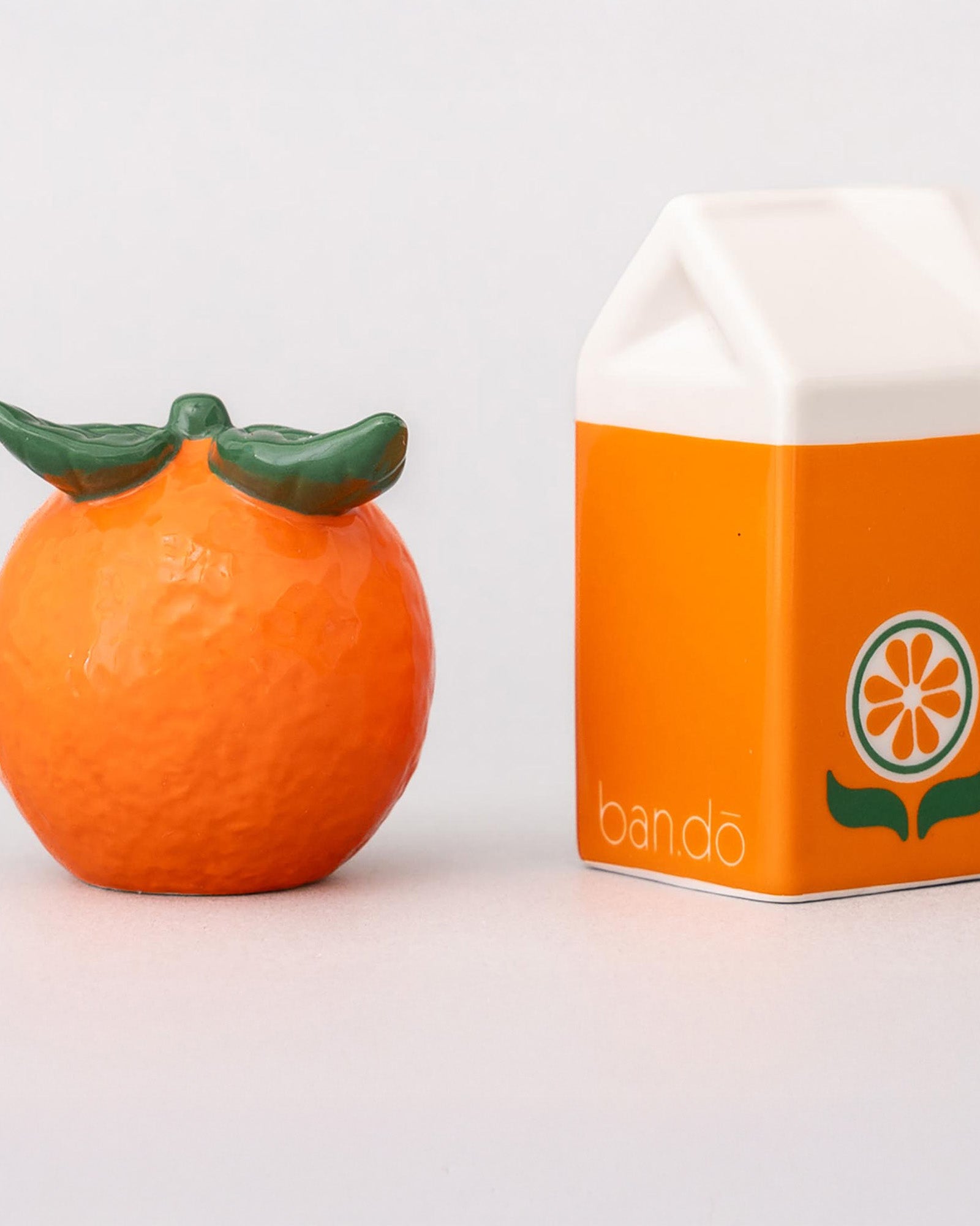 Orange-shaped container with green top next to its packaging on a white background