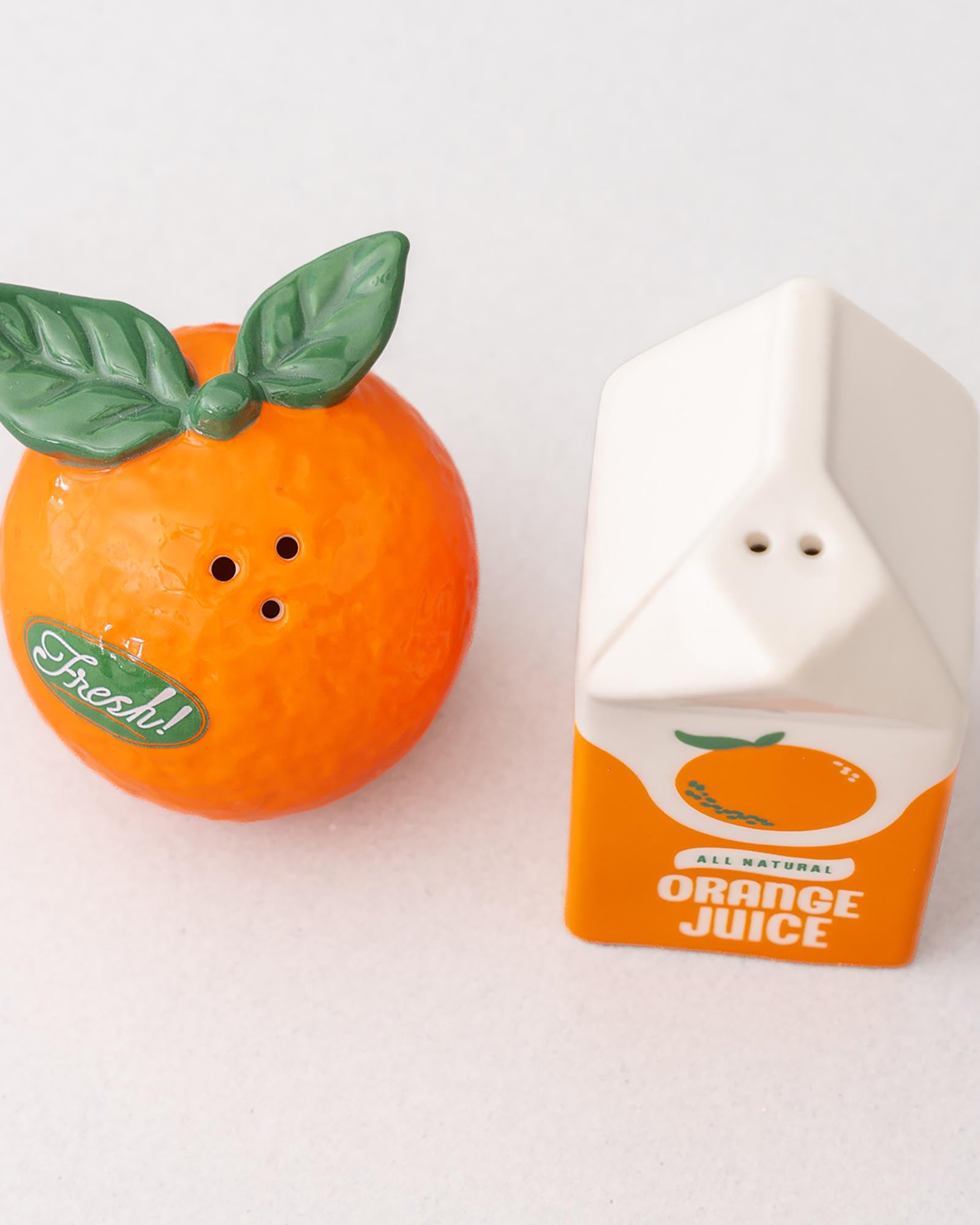 Orange-shaped salt and pepper shaker with a carton-shaped orange juice container on a white background