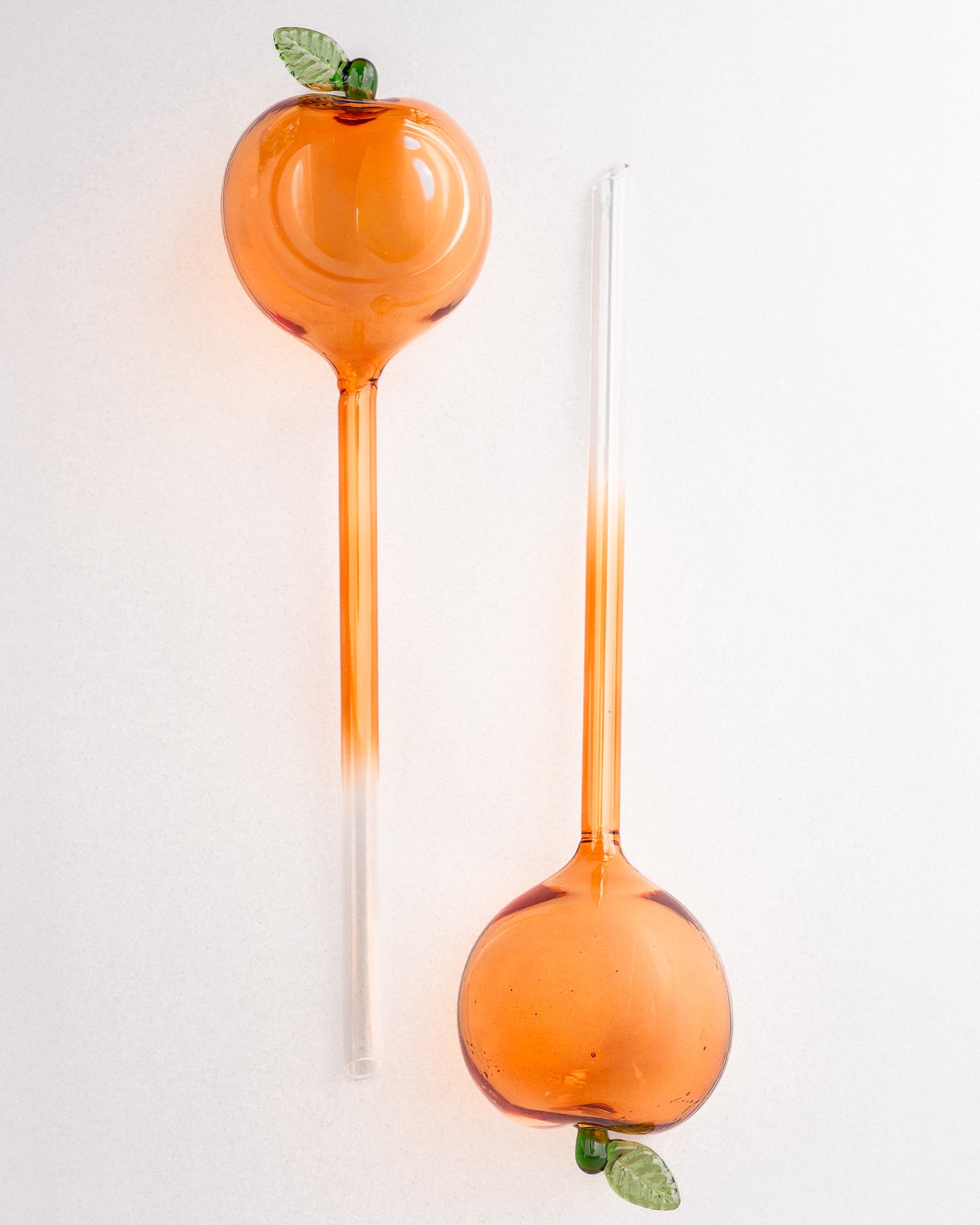 Two peach glass watering globes with green leaves on a white background