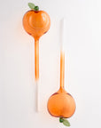 Two peach glass watering globes with green leaves on a white background