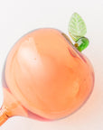 up close of Two peach glass watering globes with green leaves on a white background