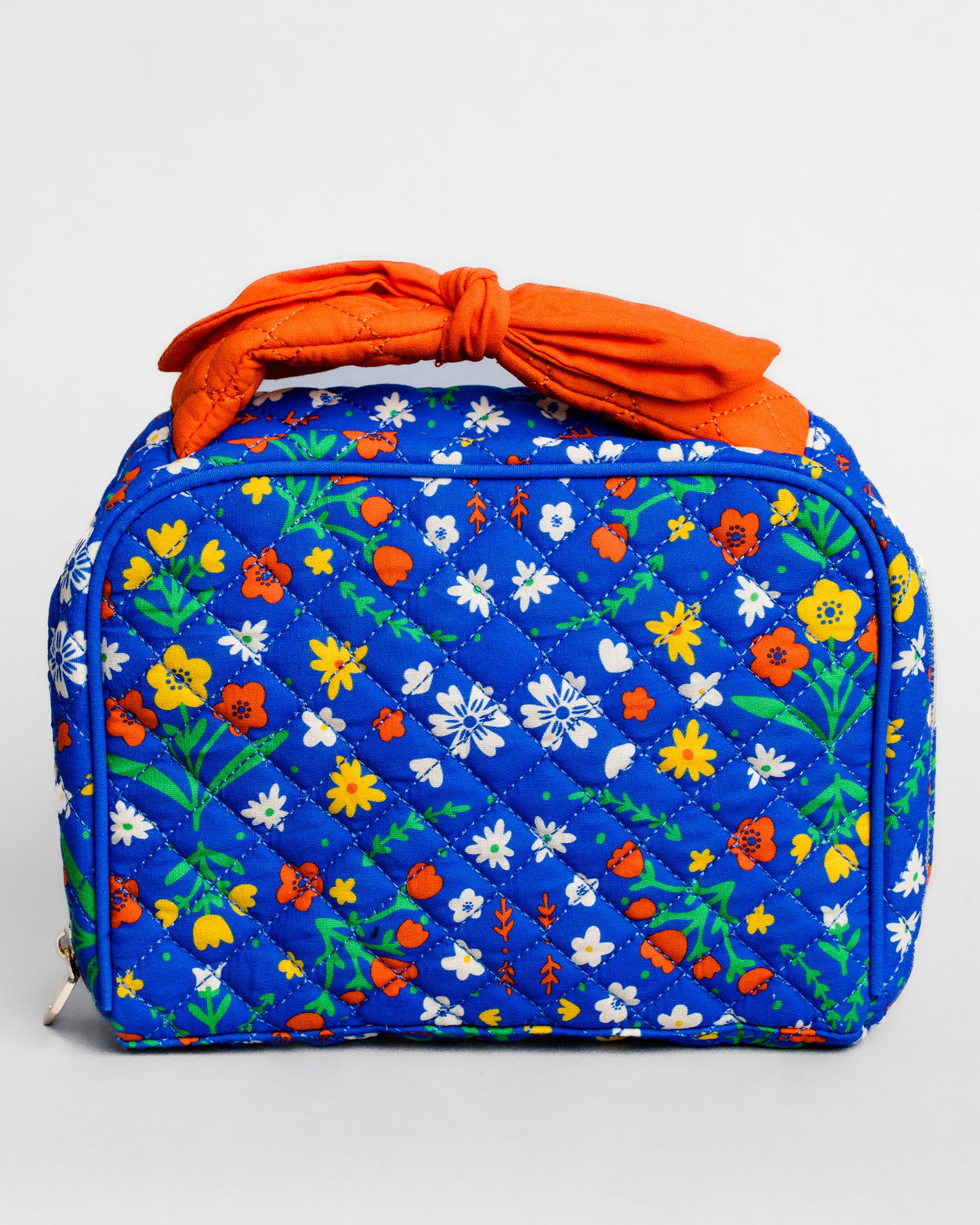 A quilted cosmetic bag with a vibrant blue background and a colorful floral print, featuring a prominent orange fabric top handle, shown on a light gray background.